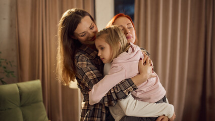 Tender family hug with two women embracing a young girl at home. Concept of emotional support, inclusivity storytelling, comforting moments, and positive modern family communication.