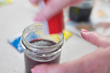 Close-up shot of a glass jar containing water, into which bright red Easter egg dye is being poured...