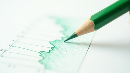 A green pencil draws a trading chart, close-up
