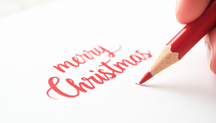 A red pencil writes merry Christmas on paper