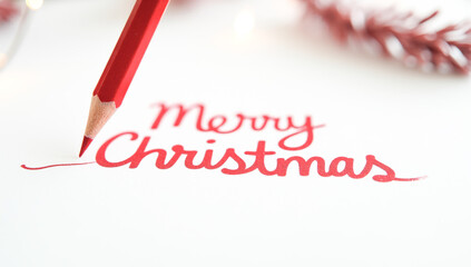 A red pencil writes merry Christmas on paper
