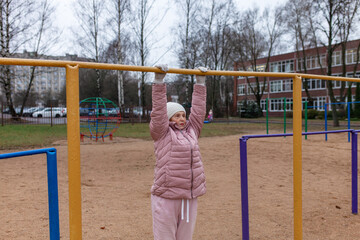Pensioner hanging on horizontal bar on playground. Senior woman exercising outdoors on colorful fitness structure. Healthy lifestyle for retirees, outdoor physical activity in city.