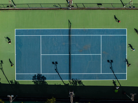 Aerial view of tennis court, where shadows stretch long across the vibrant blue and green surface, as players engage in a spirited match, Thimphu, Bhutan.