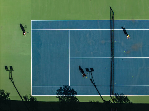 Aerial view of tennis players casting long shadows on the blue and green court, Thimphu, Bhutan.