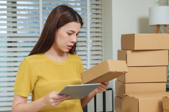 Asian businesswoman checking parcel and typing on tablet for e commerce order confirmation concept entrepreneur technology productivity modern corporate office lifestyle digital success - Powered by Adobe