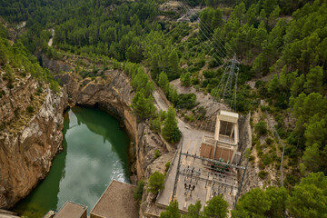Aerial view of hydroelectric facility, power lines, and rocky river gorge surrounded by dense forest in Spain.