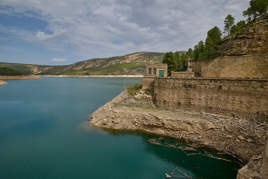 Turquoise reservoir water bordered by layered rocky cliffs and dry shoreline in a mountainous region. - Powered by Adobe