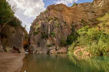 View of layered rocky canyon walls rising above green vegetation under a bright blue sky.