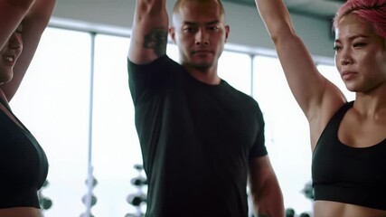 A tight medium close-up video of diverse athletes, including a plus-sized asian woman, powerfully raising interlocked hands in a modern fitness studio. Team triumph and unity concept
