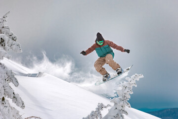 Snowboarder rides and jumps between snow capped trees at high speed. Backcountry at ski resort