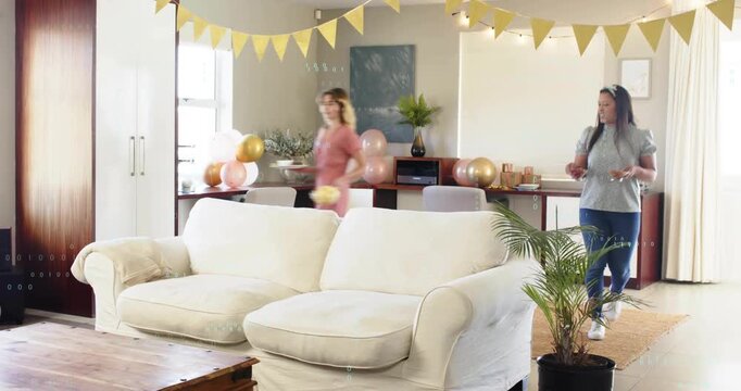 Two women initiating party setup, carrying bowl to coffee table, arranging plates under bunting