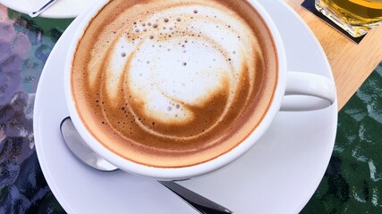 A beautiful frothy cappuccino served in a white cup on a saucer