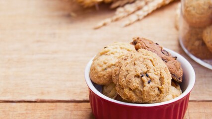 Delicious oatmeal raisin cookies in a red bowl on a wooden table
