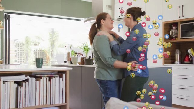 Two women embracing in kitchen leaning in and sharing love causing social media emojis rising right