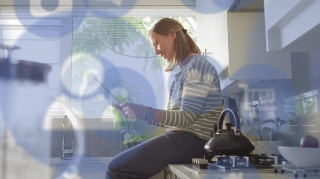 Woman sitting on counter handling green device for testing, tapping control revealing tech overlay