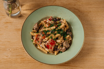 Creamy pasta with meat and vegetables on a green plate