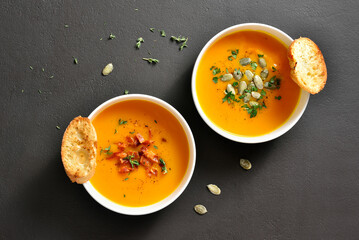 Bowls of creamy pumpkin and carrot soup with bacon and seeds