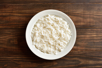 Boiled rice on plate on brown wooden background, top view