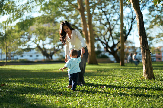 Mother guiding toddler son learning walking in park