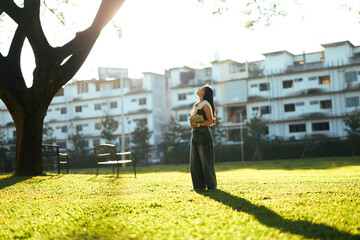 Woman holding book looking at sunlight in urban park