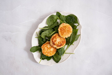 Homemade golden fish cakes served on fresh spinach leaves on a white plate, top view, simple and clean food presentation.