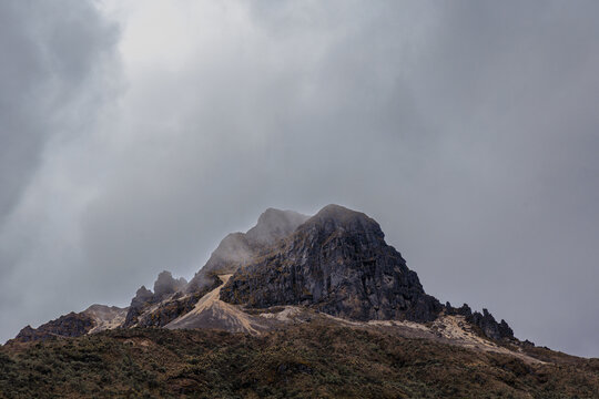 Cumbre rocosa del P&aacute;ramo Andino emergiendo bajo una densa capa de niebla, mostrando la &aacute;rida vegetaci&oacute;n de altura y el dramatismo del clima en Los Nevados.