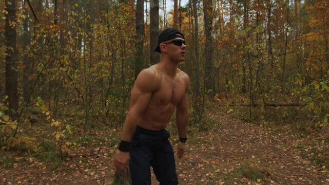 Young muscular shirtless man performs squats in an autumn forest clearing covered with yellow leaves. Calisthenics.