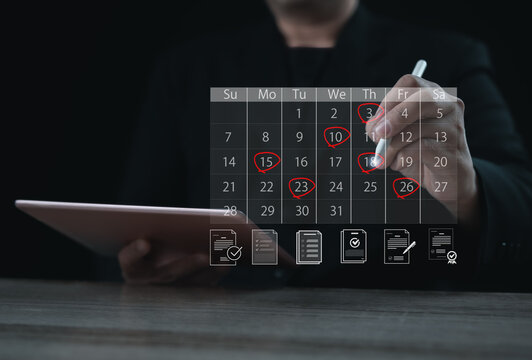 A planner marking important dates on a digital calendar using a stylus while holding a tablet. The highlighted days represent scheduling, organization, time management, reminders, and deadline prepara