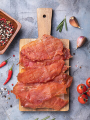 A top view of slices of dried chicken meat on a wooden tray, surrounded by various spices