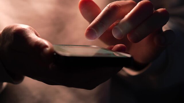 A close-up of a man holding a touchscreen phone in the dark.
Backlight on the smartphone display.
Gadget phone, smartphone, messaging, sending SMS