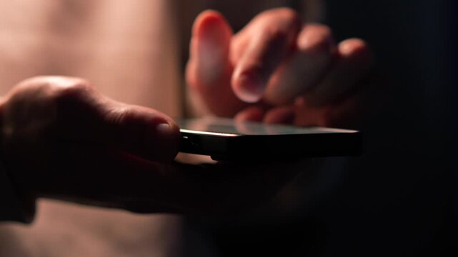 A close-up of a man holding a touchscreen phone in the dark.
Backlight on the smartphone display.
Gadget phone, smartphone, messaging, sending SMS
