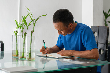 Man writing at glass dining table with bamboo, focused, taking notes, left hand missing four fingers visible