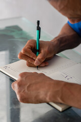 Close crop of hands and pen writing in planner, clear view of left hand missing four fingers, detailed shot