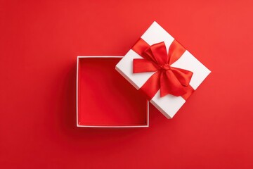 Overhead view of an open white gift box with a red ribbon and bow on a vibrant red background