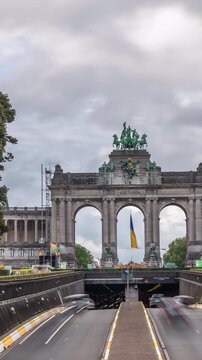 Timelapse of the Cinquantenaire Arcade in Jubelpark, Brussels, Belgium. The memorial triumphal arch stands tall under dramatic clouds, symbolizing Belgian history and independence. Traffic in a tunnel