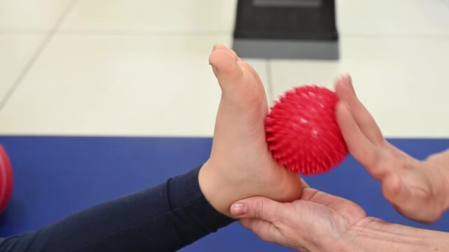 A physical therapist massages a child's foot with a massage ball to rehabilitate flat feet. Sensory stimulation for children: close-up of a hand and foot.
