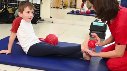 A physical therapist massages a child's foot with a massage ball to rehabilitate flat feet. Sensory stimulation for children