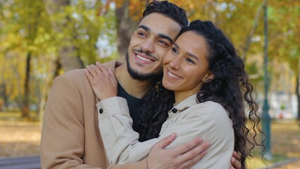 Close-up happy hispanic couple smiling toothy hugging cuddling in autumn park closeness love bonding Arabian family hug cuddle in city outdoors smile looking away married man with woman autumnal fall