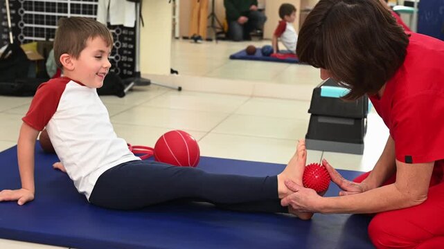 A physical therapist massages a child's foot with a massage ball to rehabilitate flat feet. Sensory stimulation for children