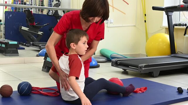 A physical therapist works with a child on posture exercises. A woman professional osteopath helps a boy do exercises to combat scoliosis.