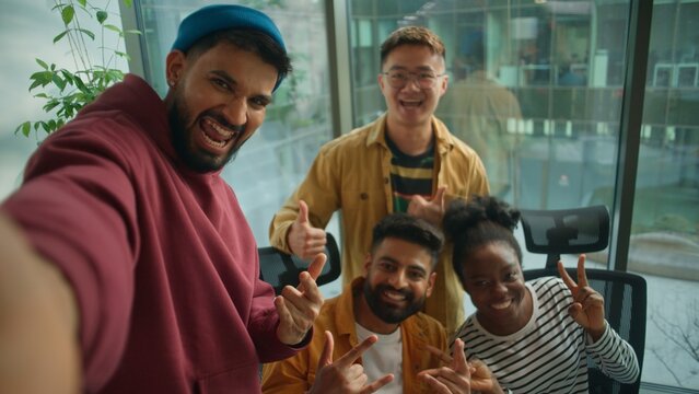Business casual startup team in office meeting joy fun smiling making selfie photo together enjoying teamwork in friendly coworking posing for video call vlog take picture multiethnic four people