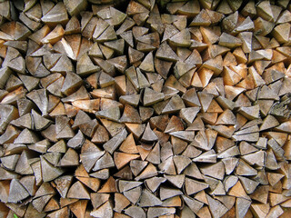 Stacked chopped firewood forms a dense geometric pattern of natural wood textures, natural background.