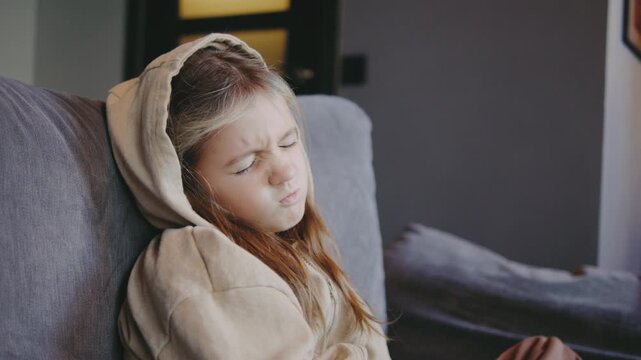 Girl with a sad expression sitting on a couch, lost in thought during a quiet moment indoors