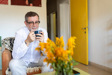 Middle-aged man in glasses enjoying a hot beverage while sitting in an armchair at home