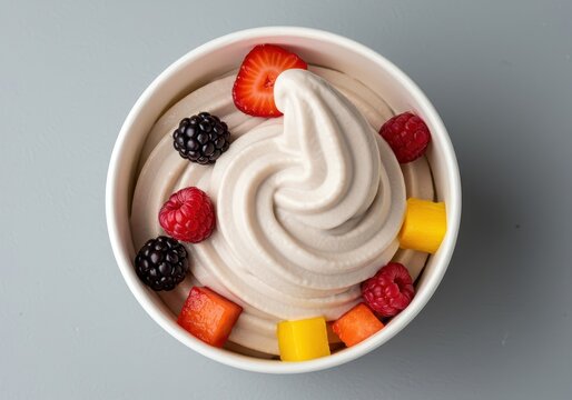 A swirl of creamy frozen yogurt dessert topped with fresh berries and colorful fruit pieces in a white serving cup, photographed close up ,raspberry ,topping ,soft serve