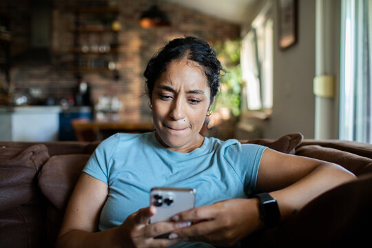 Adult woman looking concerned at smartphone on sofa at home