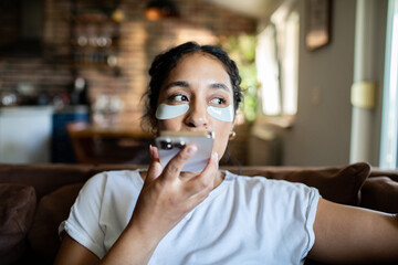 Young adult woman relaxed with eye patches using phone at home