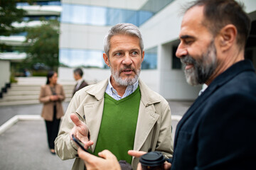 Mature businessmen having focused conversation outside office building