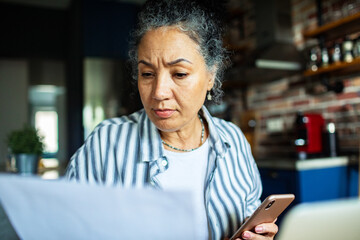 Mature woman worried reviewing bills in home kitchen