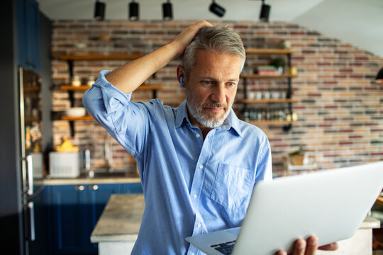 Mature man looking confused at laptop in home kitchen